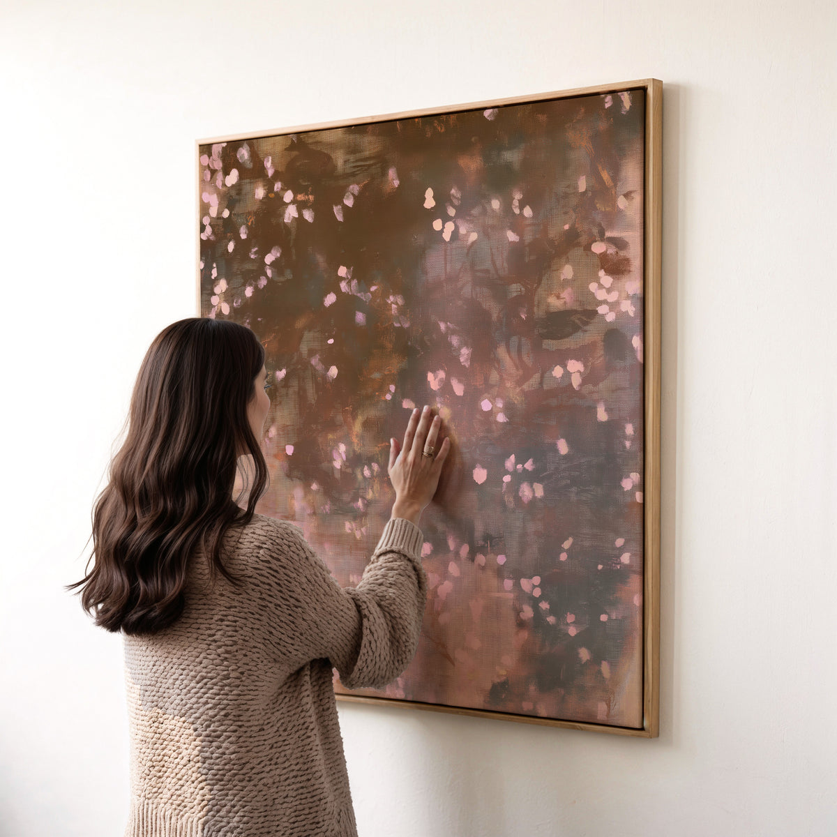 Framed square canvas art, earthy brown moody botanical print Oaken Petal No. 1124 shown with a person gently touching the tactile matte cotton-blend canvas and custom wood float frame