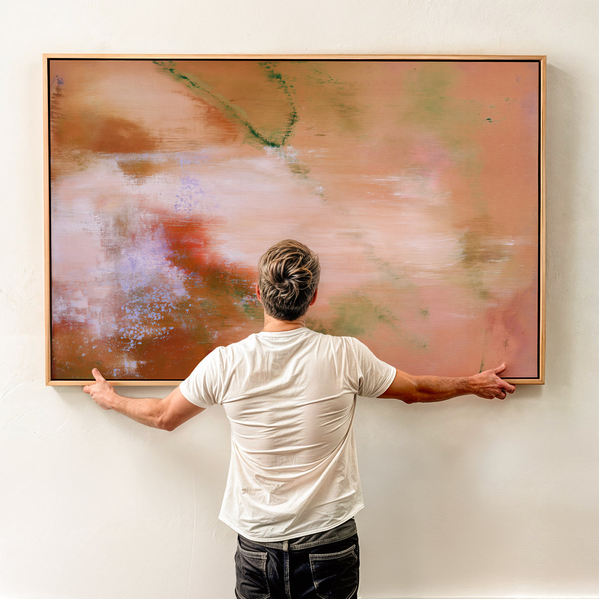 Person holding a large horizontal framed terracotta abstract canvas art print against a light wall to demonstrate scale.
