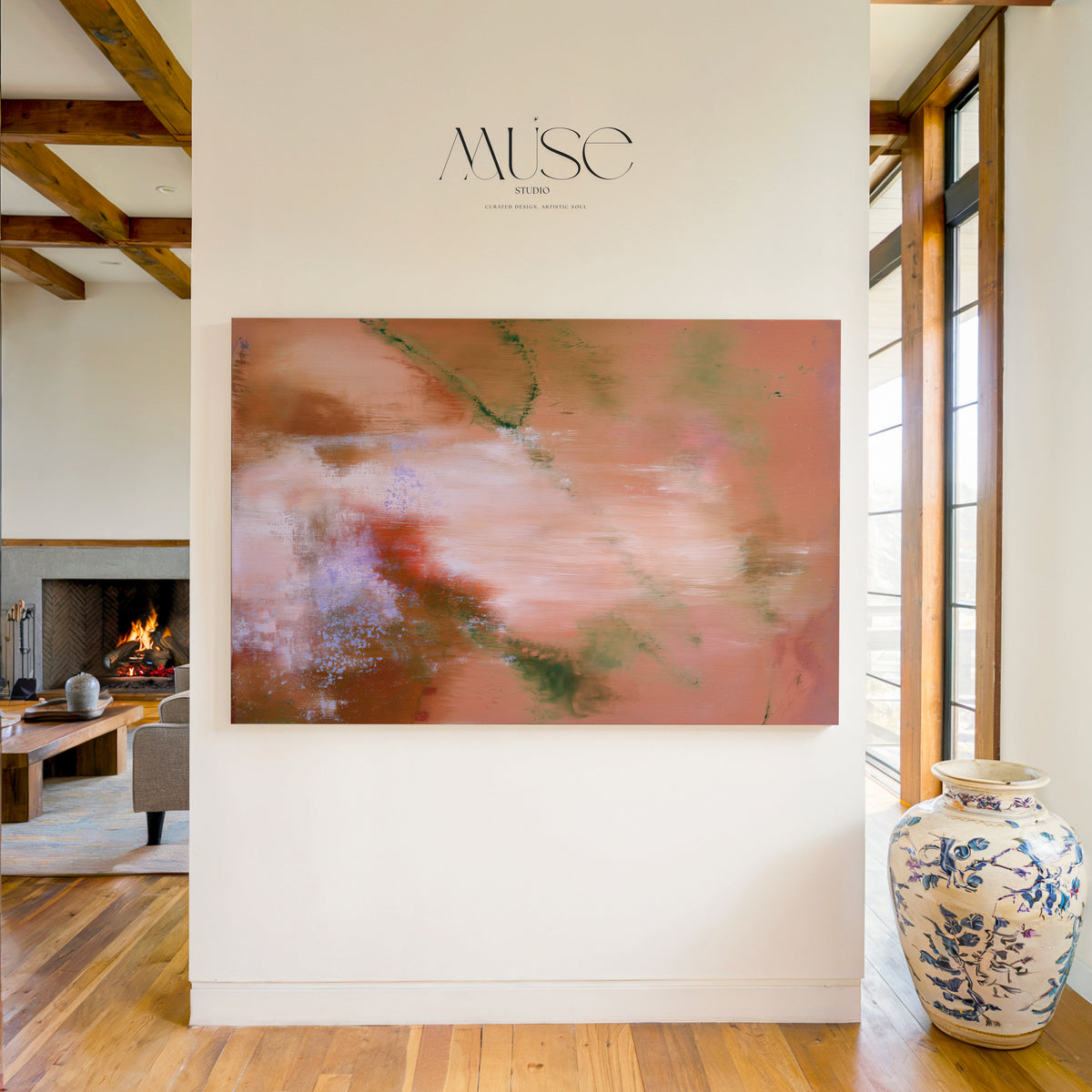 An abstract canvas painting with pink, terracotta, and green brushstrokes displayed on a white wall in a modern home interior. The brand name 'MUSE ART' is printed above the artwork, and a blue-and-white ceramic vase sits on the wooden floor to the right.
