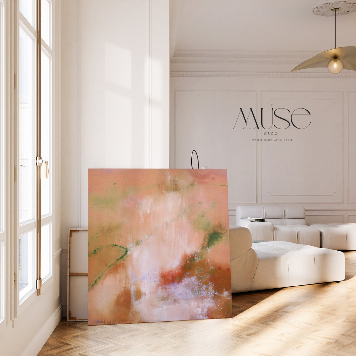 Large square abstract canvas leaning against a wall in an airy European apartment featuring herringbone wood floors, french windows, and a low white leather sectional.