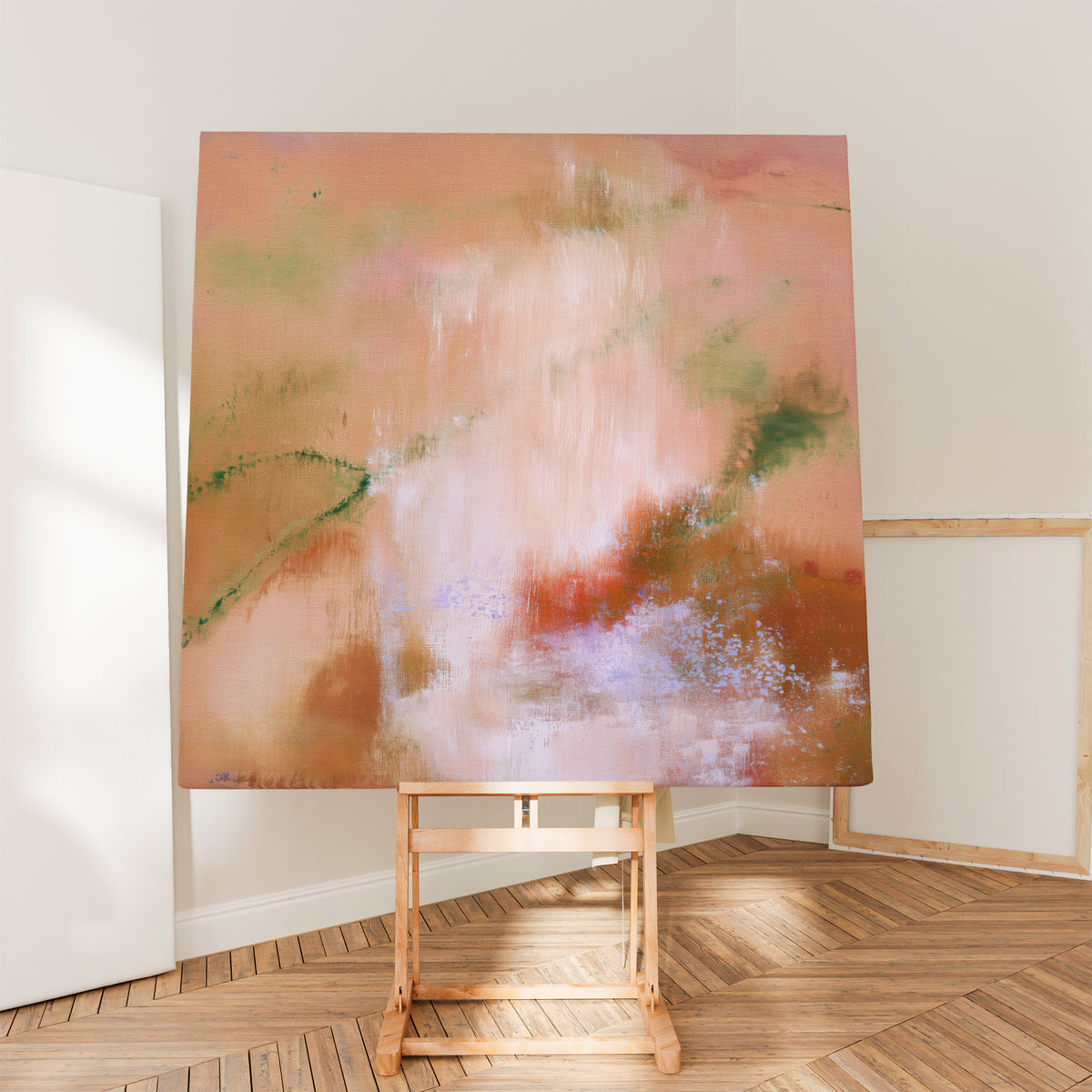 Square abstract canvas painting resting on a wooden artist easel inside a sunlit creative studio with chevron parquet wood floors.   