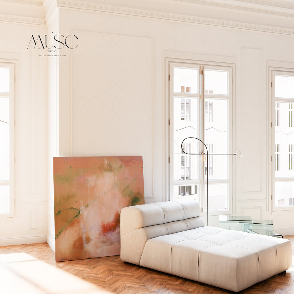 Oversized square artwork leaning against a white wall next to a modern cream tufted chaise lounge sofa and tall french windows.