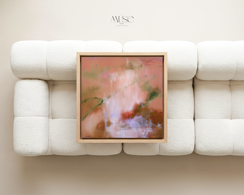 Framed square terracotta abstract canvas art in a light oak frame resting on a plush white bouclé sofa.