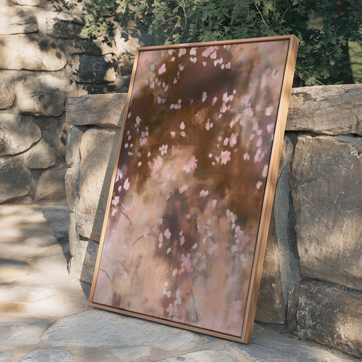 Framed abstract canvas Dawn Nocturne No. 1123 leaning against a rustic natural stone retaining wall in warm sunlight with leafy foliage overhead.