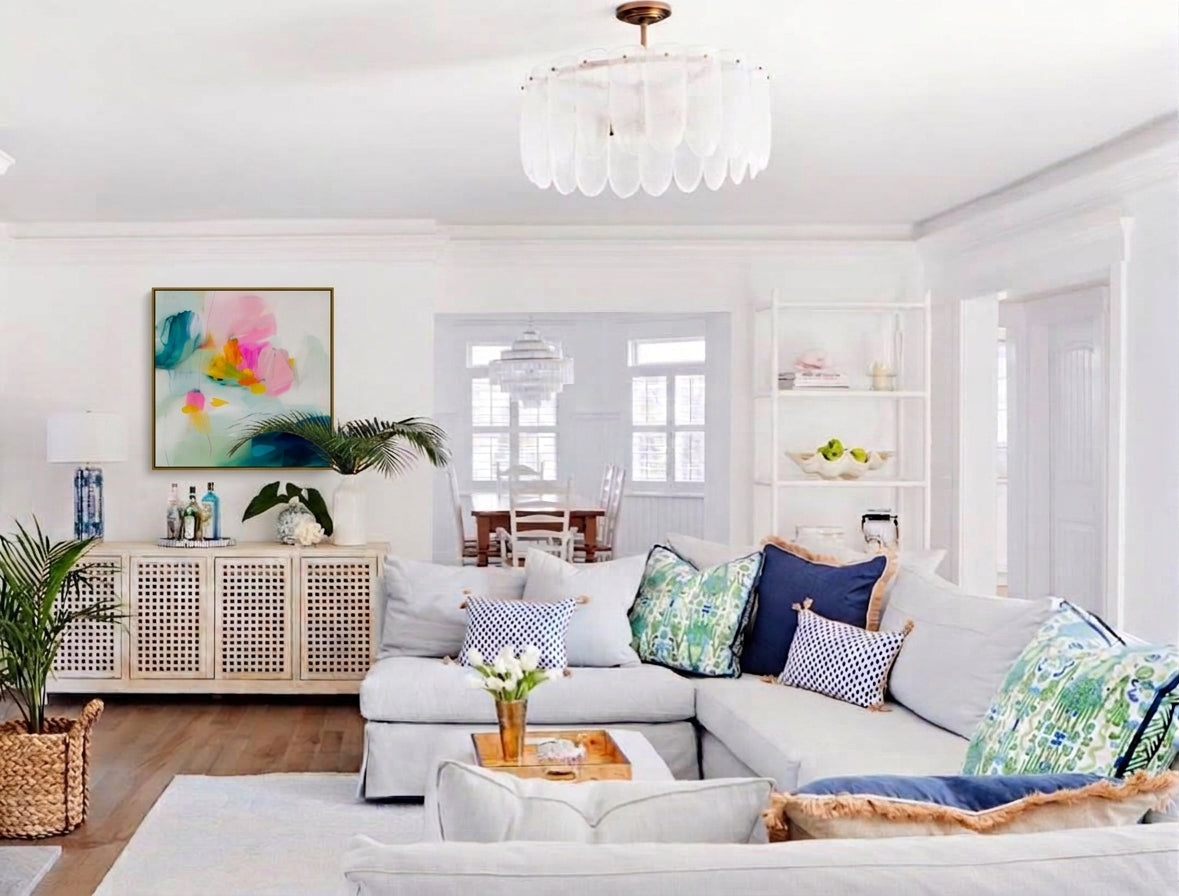 Vibrant abstract floral wall art framed above a white sideboard cabinet in a modern coastal living room with blue accent pillows and palm decor.