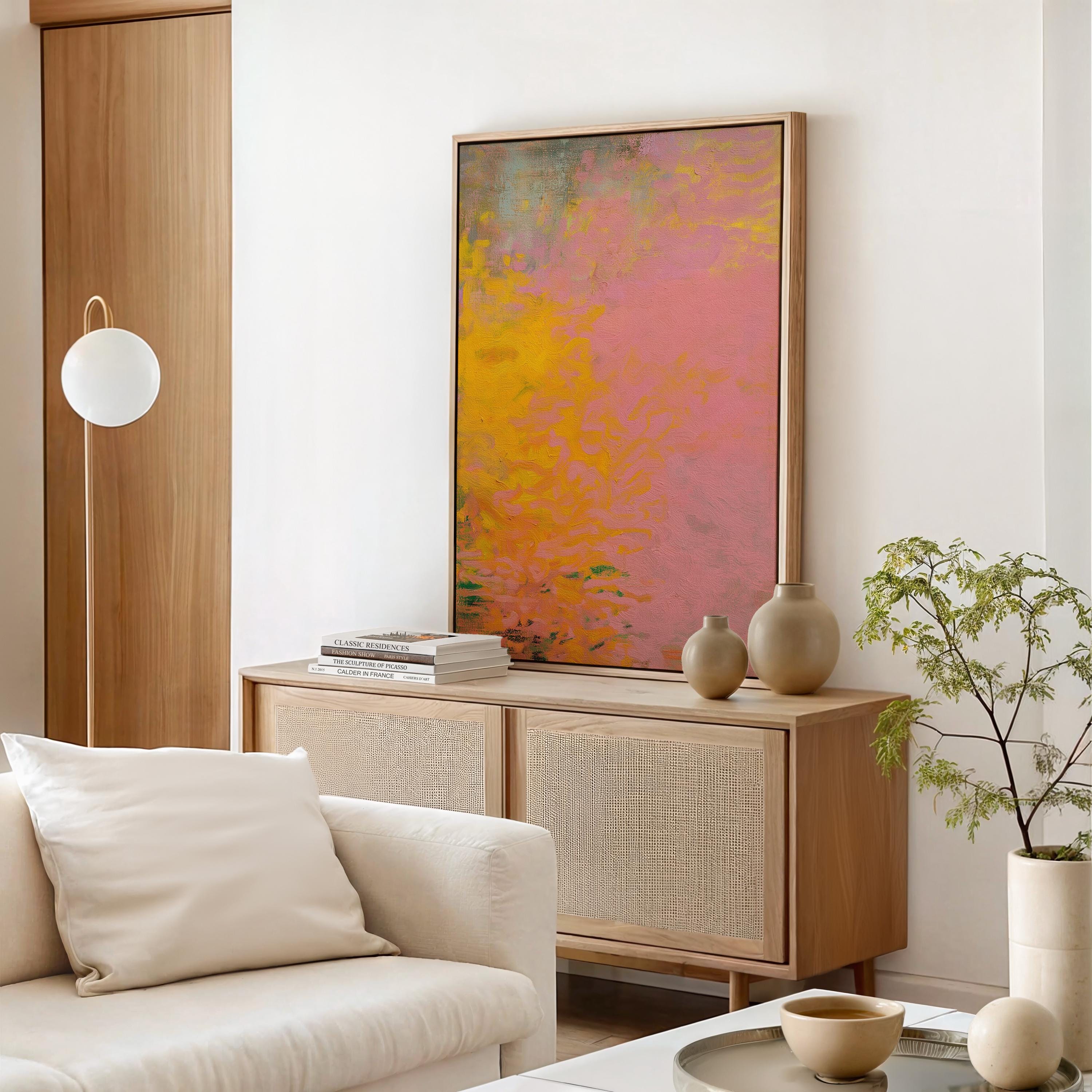 Vertical framed canvas wall art featuring a bold abstract blend of pink, orange, and yellow tones. The textured gradient evokes sunset warmth and modern earthiness, styled here in a neutral living room with wood furniture, clean lines, and soft minimal accents. Ideal for entryways, minimalist interiors, or natural modern decor spaces seeking a colorful yet refined focal piece.