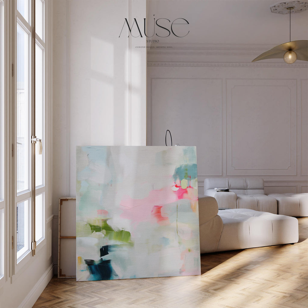 Framed abstract canvas wall art in blush pink, blue, green, and soft neutral tones. Square modern painting with expressive brushstrokes and light color palette. Ideal for bedrooms, home offices, or styled spaces seeking a feminine and fresh decor piece. Presented in a natural wood frame, this soft contemporary artwork adds gentle movement and colorful balance to curated interiors. A Muse Studio original designed for designer-led spaces.