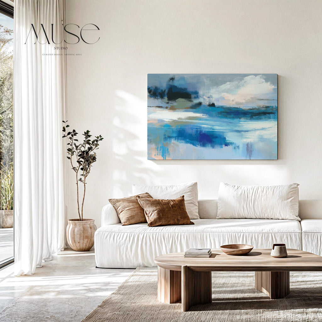 Oversized blue coastal abstract wall art with soft white clouds and ocean-inspired brushstrokes, leaning against paneled walls in a sunlit room. Muted coastal horizon artwork available as framed wall art, canvas, or fine art print by Muse Studio.