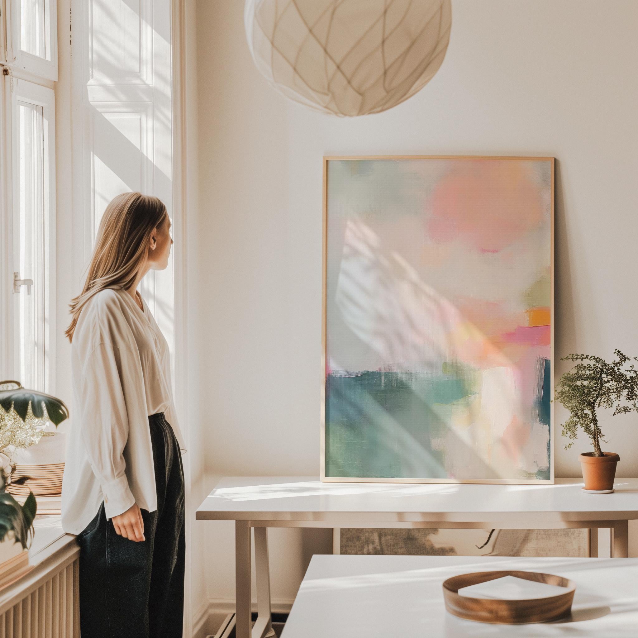 Framed giclée poster print of a soft blush and sage abstract with peach, coral, and teal tones in a vertical layout. Displayed in a light-filled modern interior with natural wood accents. Available as a fine art poster or canvas wall art for curated, color-forward decor.