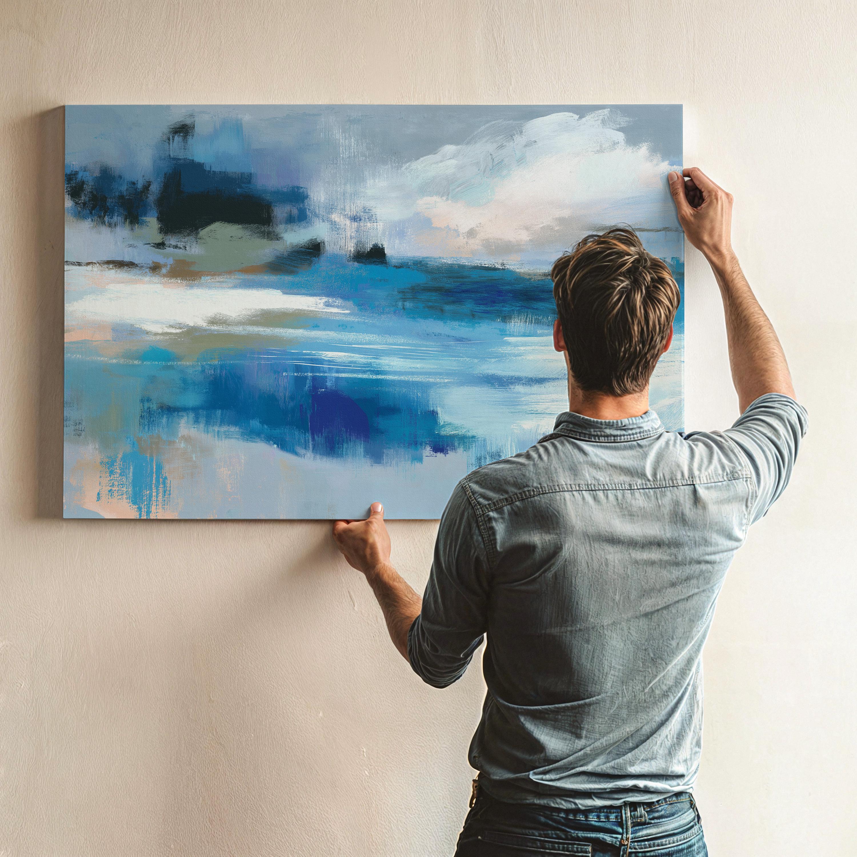 Oversized blue coastal abstract wall art with soft white clouds and ocean-inspired brushstrokes, leaning against paneled walls in a sunlit room. Muted coastal horizon artwork available as framed wall art, canvas, or fine art print by Muse Studio.