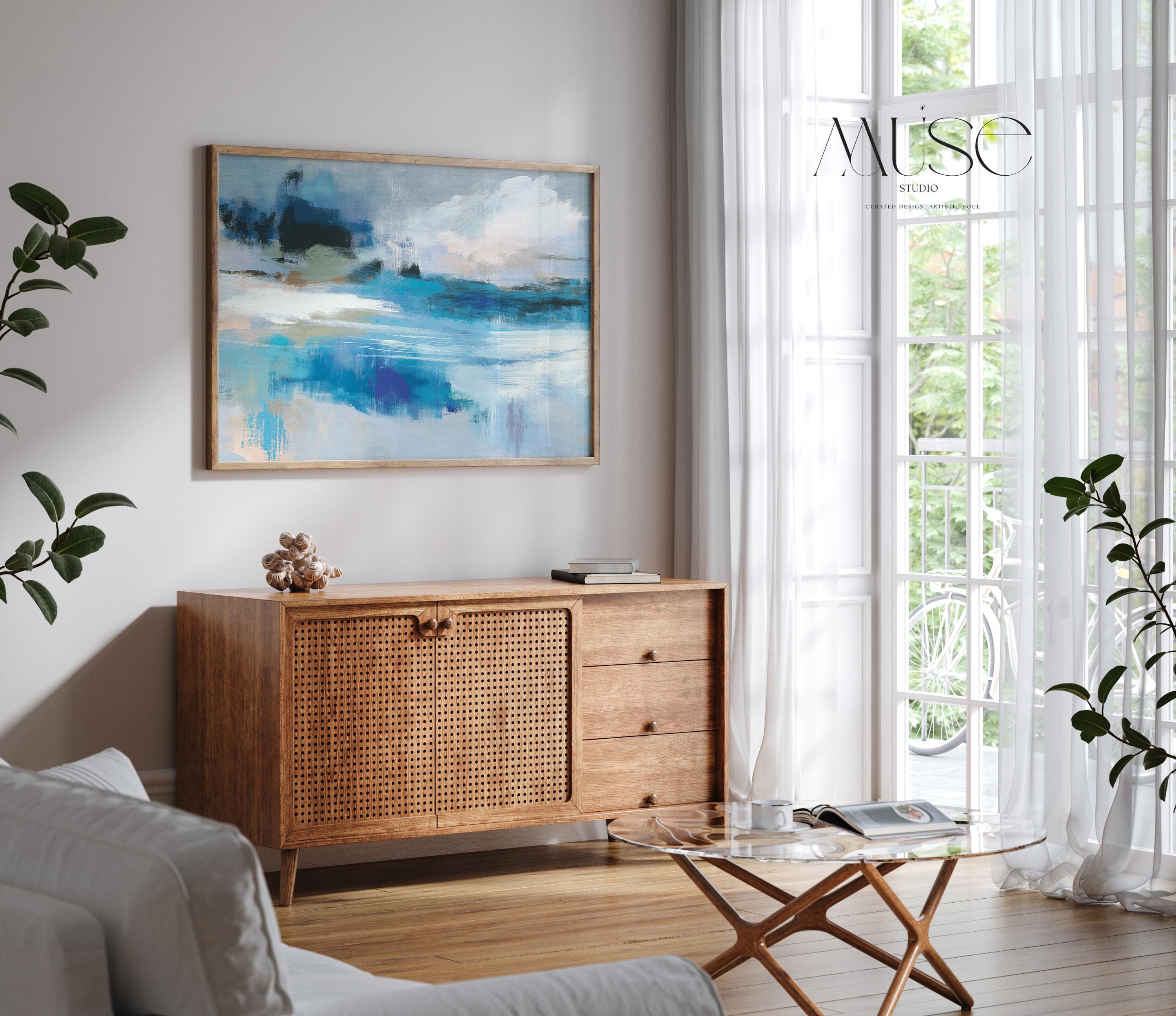 Oversized blue coastal abstract wall art with soft white clouds and ocean-inspired brushstrokes, leaning against paneled walls in a sunlit room. Muted coastal horizon artwork available as framed wall art, canvas, or fine art print by Muse Studio.