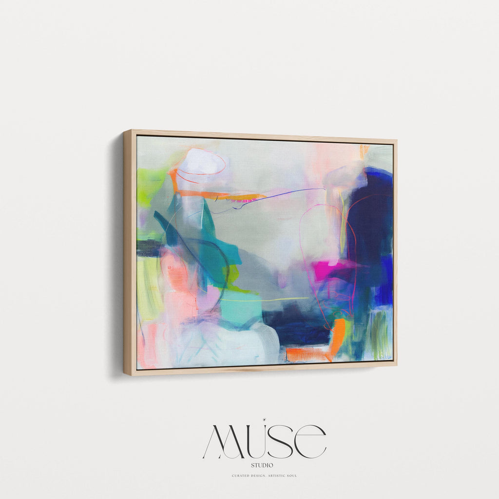Large horizontal abstract wall art in bright blue, neon pink, teal, and multicolor tones displayed above a white sofa in a modern neutral living room with natural light and minimal decor. Vibrant color pop artwork available as framed canvas or fine art print by Muse Studio.