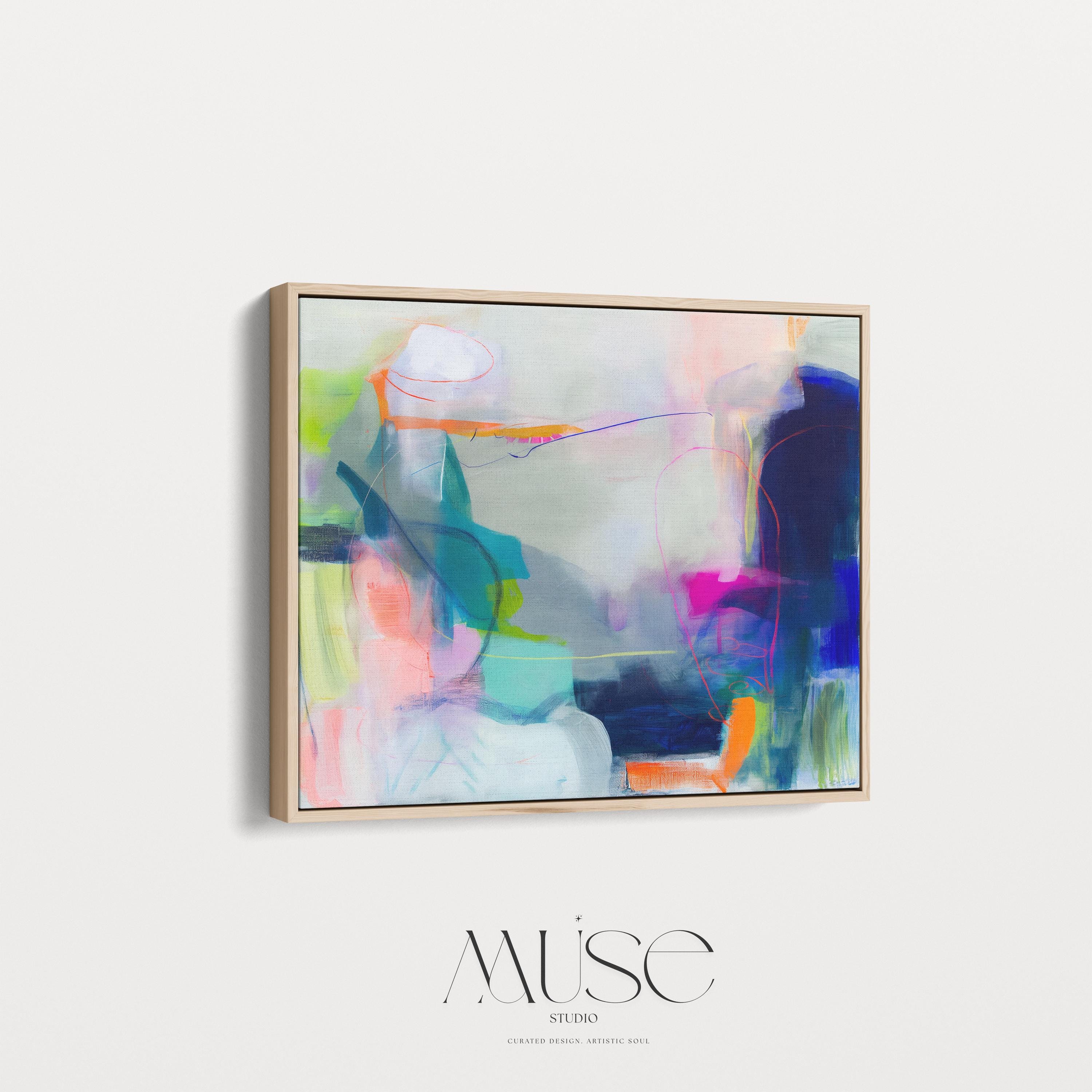 Large horizontal abstract wall art in bright blue, neon pink, teal, and multicolor tones displayed above a white sofa in a modern neutral living room with natural light and minimal decor. Vibrant color pop artwork available as framed canvas or fine art print by Muse Studio.