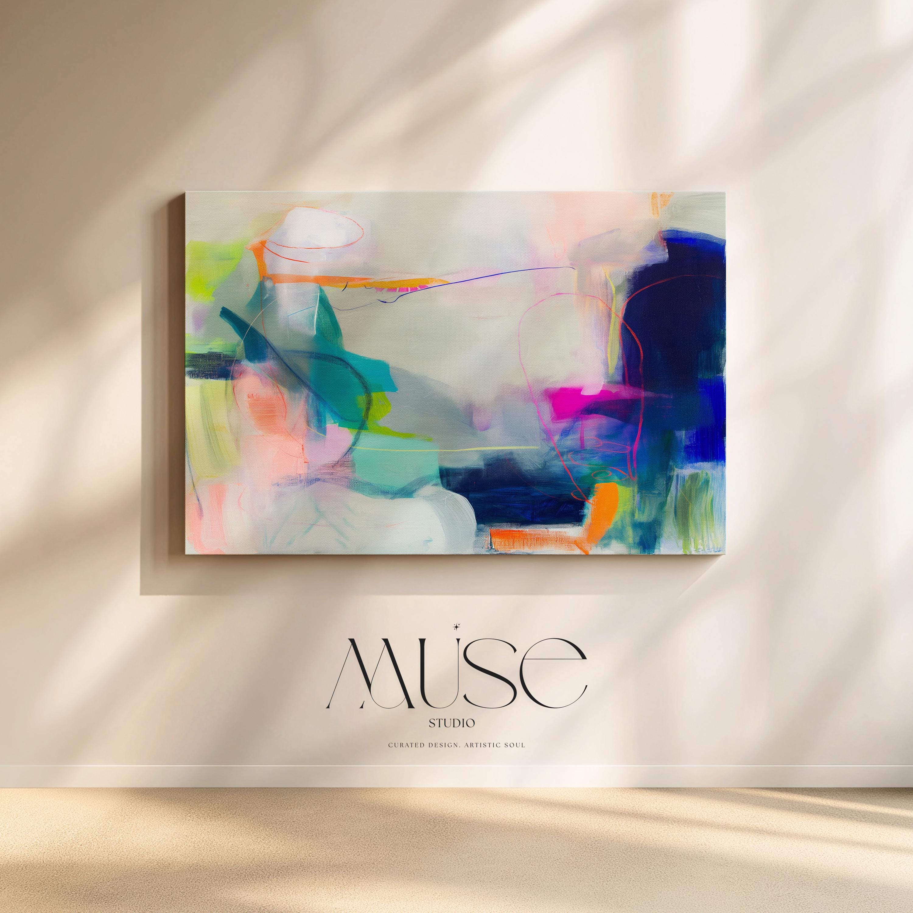 Large horizontal abstract wall art in bright blue, neon pink, teal, and multicolor tones displayed above a white sofa in a modern neutral living room with natural light and minimal decor. Vibrant color pop artwork available as framed canvas or fine art print by Muse Studio.