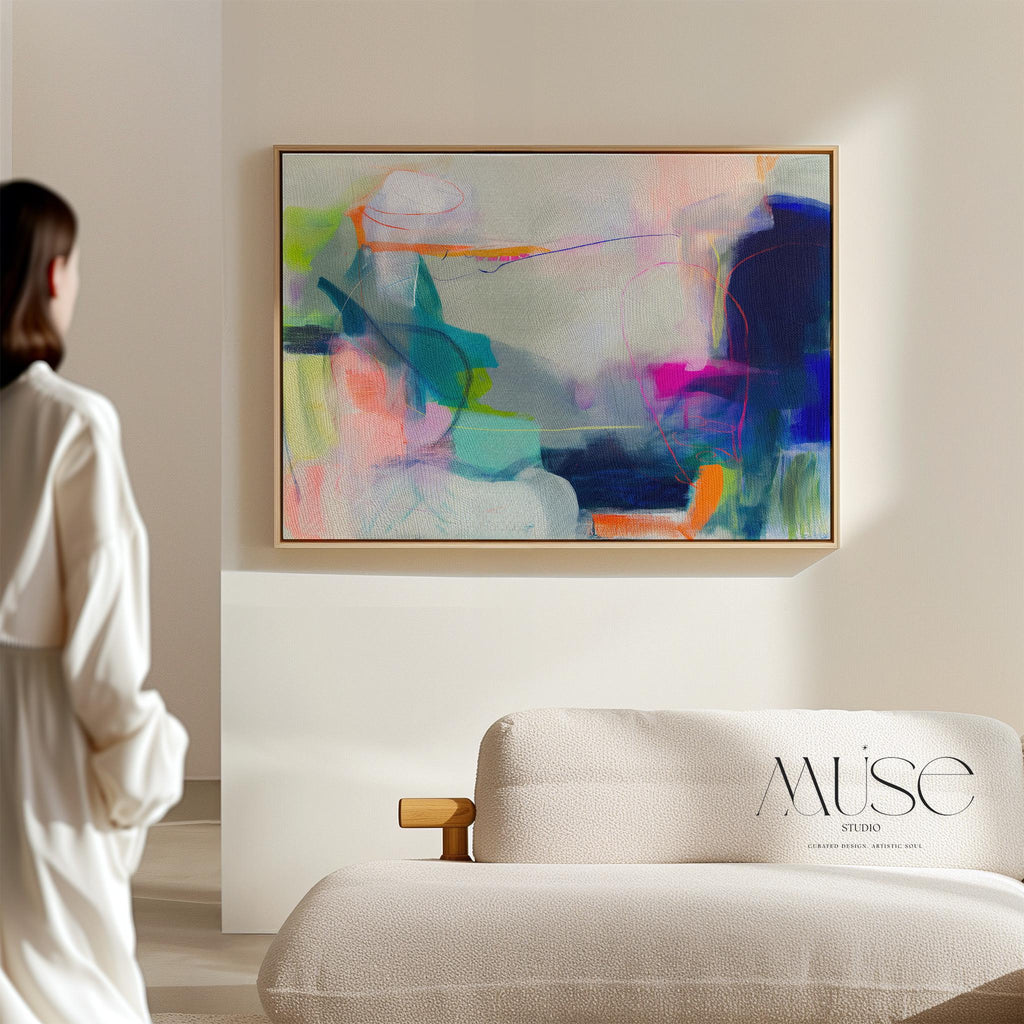 Large horizontal abstract wall art in bright blue, neon pink, teal, and multicolor tones displayed above a white sofa in a modern neutral living room with natural light and minimal decor. Vibrant color pop artwork available as framed canvas or fine art print by Muse Studio.