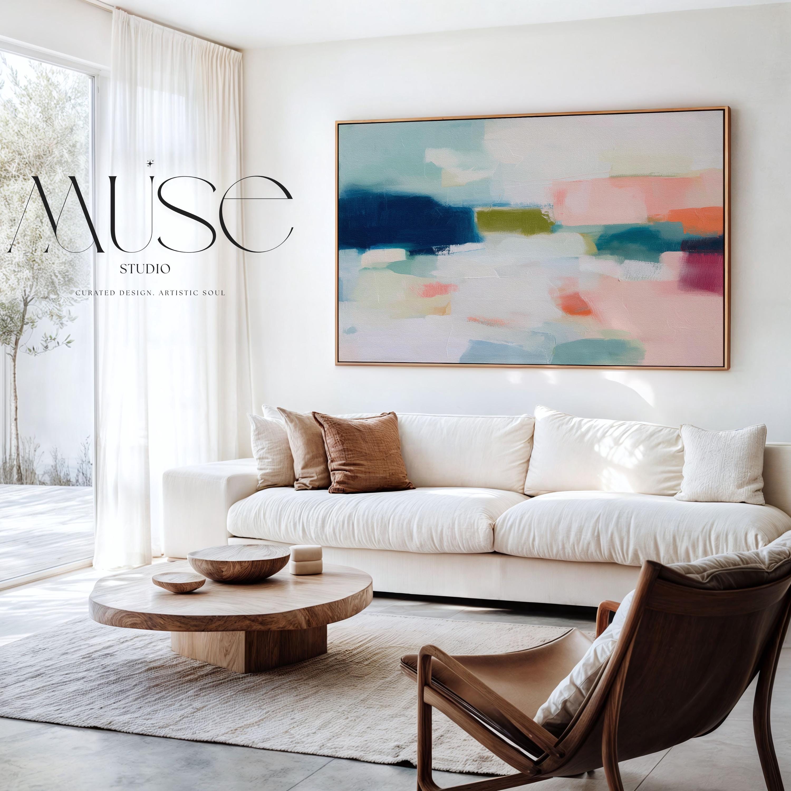 Large horizontal abstract framed canvas wall art featuring deep navy blue, muted aqua, soft blush pink, olive green, coral accents, and layered white brushstrokes, styled above a neutral sofa in a modern coastal living room, offering balanced contrast and refined contemporary color.