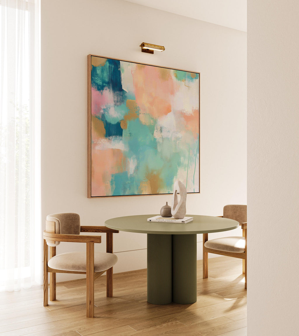 Large square abstract framed canvas wall art featuring coral, peach, teal, aqua blue, and warm sand tones layered over a soft cream background, styled above a neutral sofa, adding soft color contrast and airy painterly texture to a curated living space.