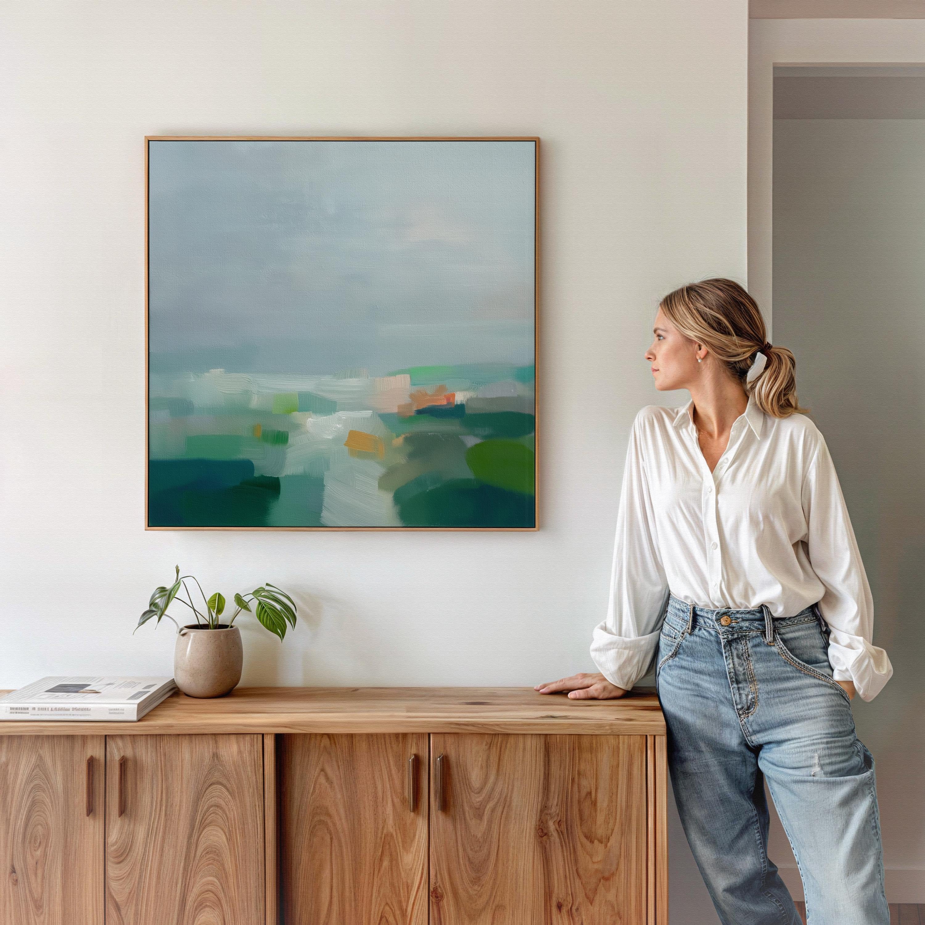Large square abstract decor wall art featuring mist blue, sea glass green, and soft teal tones, framed in natural wood and styled in a calm contemporary living room, creating a serene coastal-inspired focal point for spacious interiors.