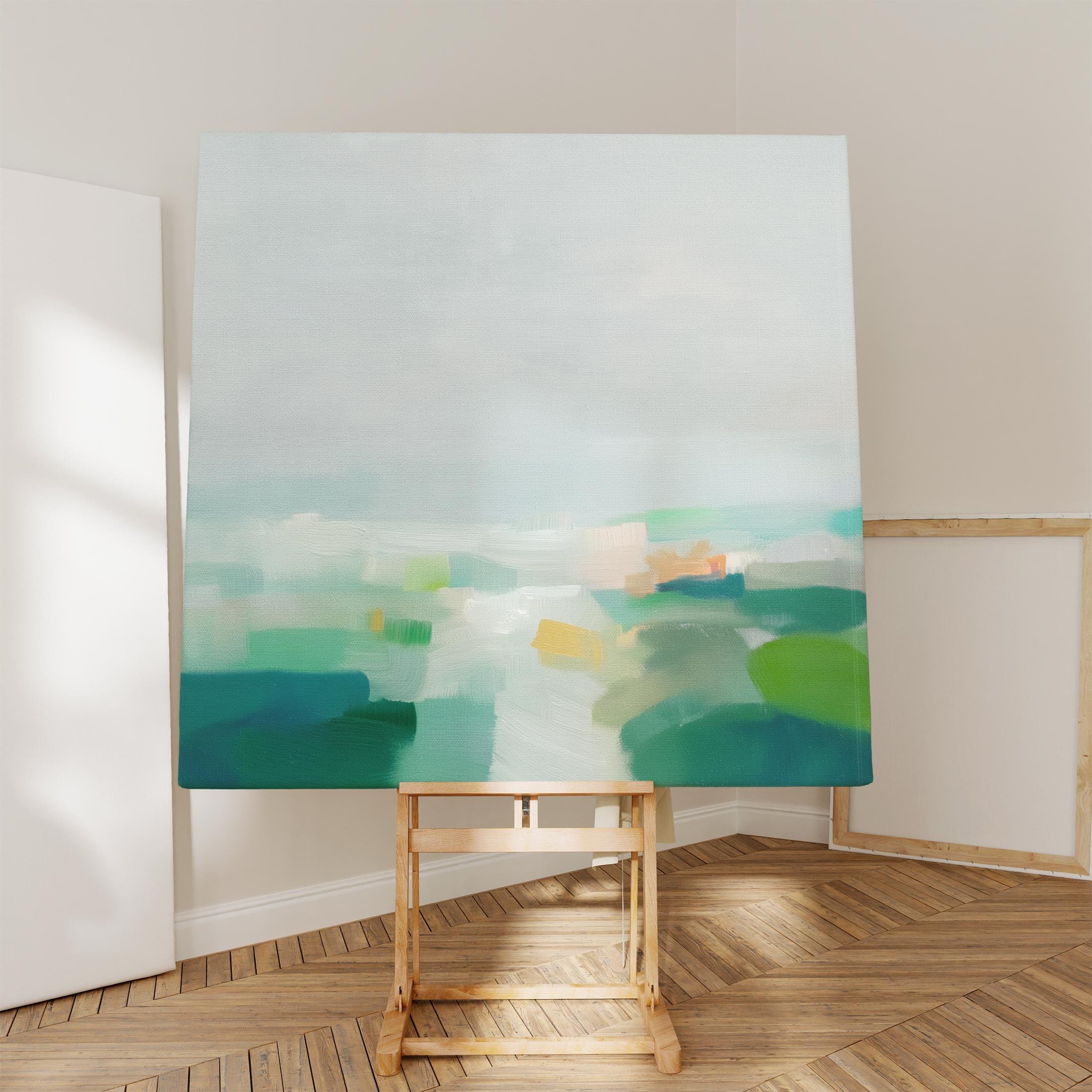 Large square stretched canvas wall art in layered sage, forest green, and soft blue tones styled in a light farmhouse interior, adding calm countryside color and gentle horizon depth to neutral walls.
