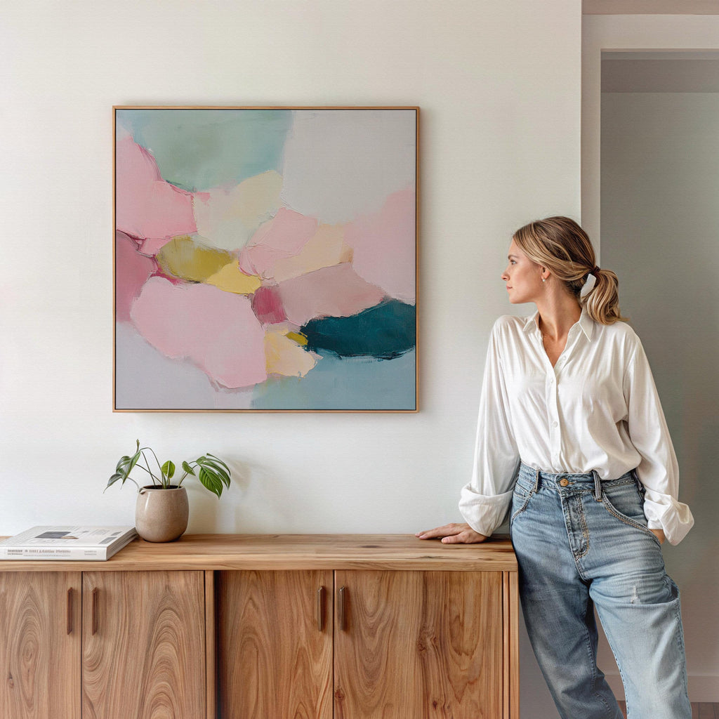 Large square abstract framed canvas wall art featuring soft blush pink, muted teal, pale aqua blue, and butter yellow painterly shapes with visible texture, styled in a modern neutral living room, offering calm color contrast and quiet luxury for above sofa or bedroom wall placement.