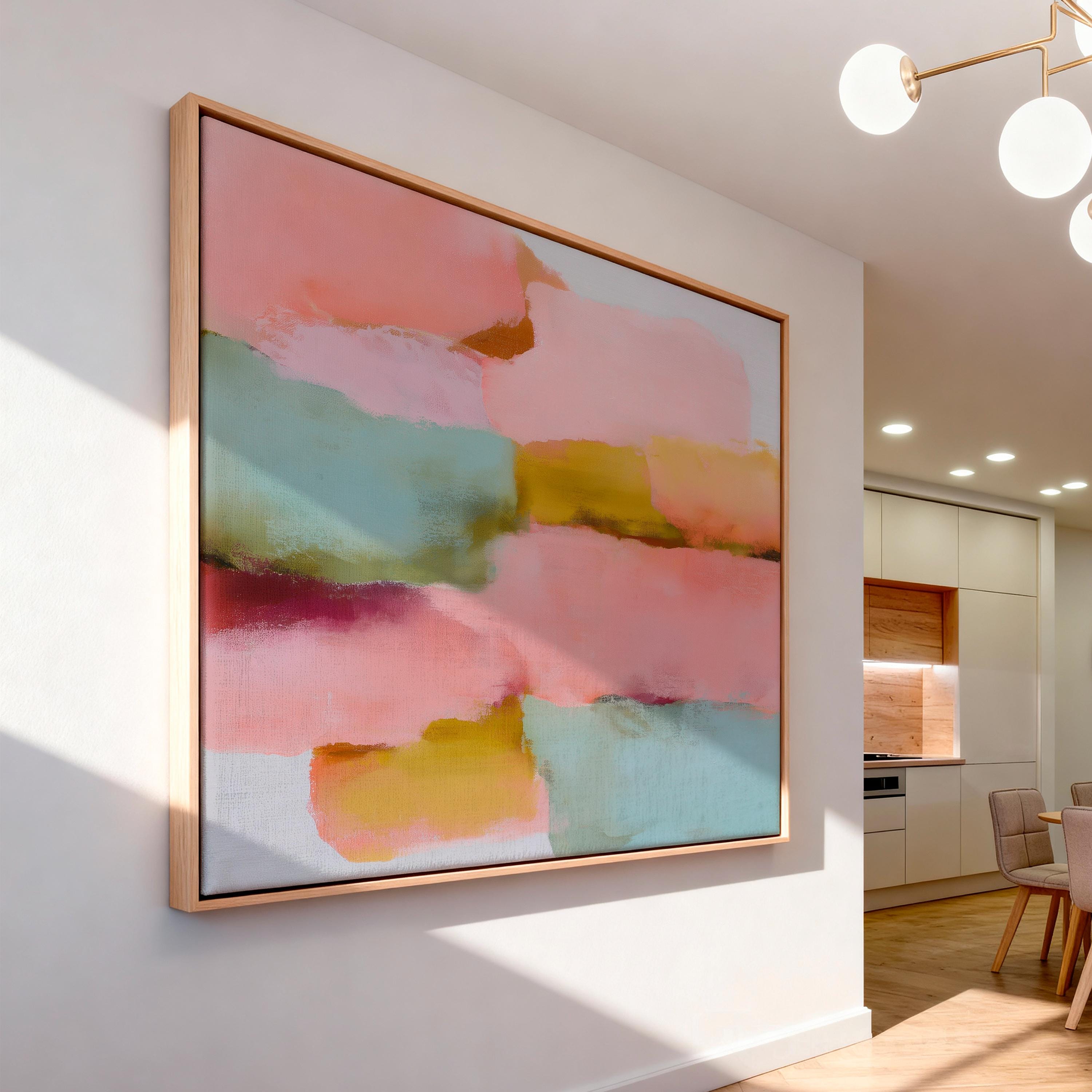 Large horizontal abstract framed canvas wall art featuring blush pink, coral, muted aqua blue, golden ochre, and plum layered brushstrokes, styled above a neutral sofa in a modern living room, offering warm contemporary color and balanced movement for oversized wall placement.