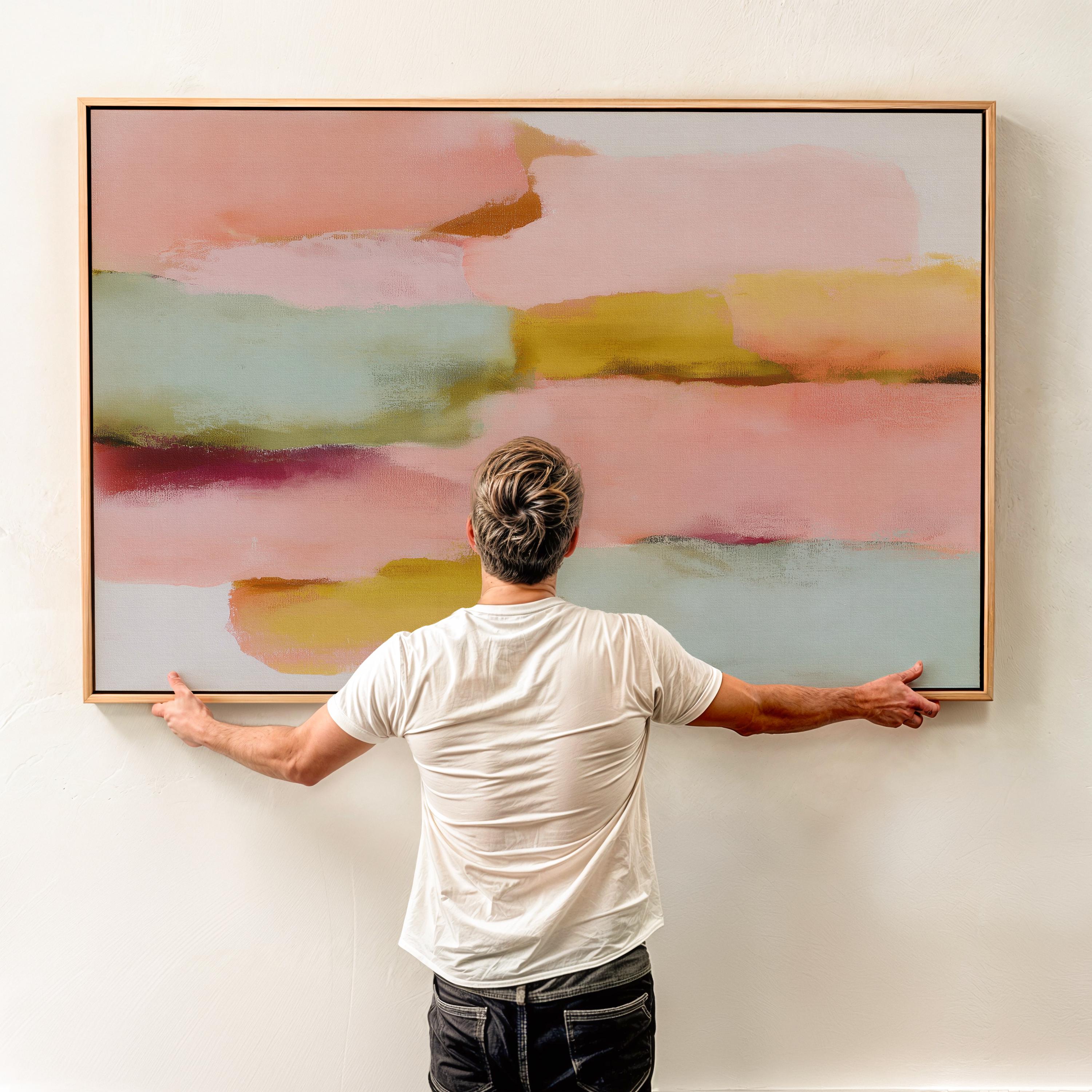 Large horizontal abstract framed canvas wall art featuring blush pink, coral, muted aqua blue, golden ochre, and plum layered brushstrokes, styled above a neutral sofa in a modern living room, offering warm contemporary color and balanced movement for oversized wall placement.