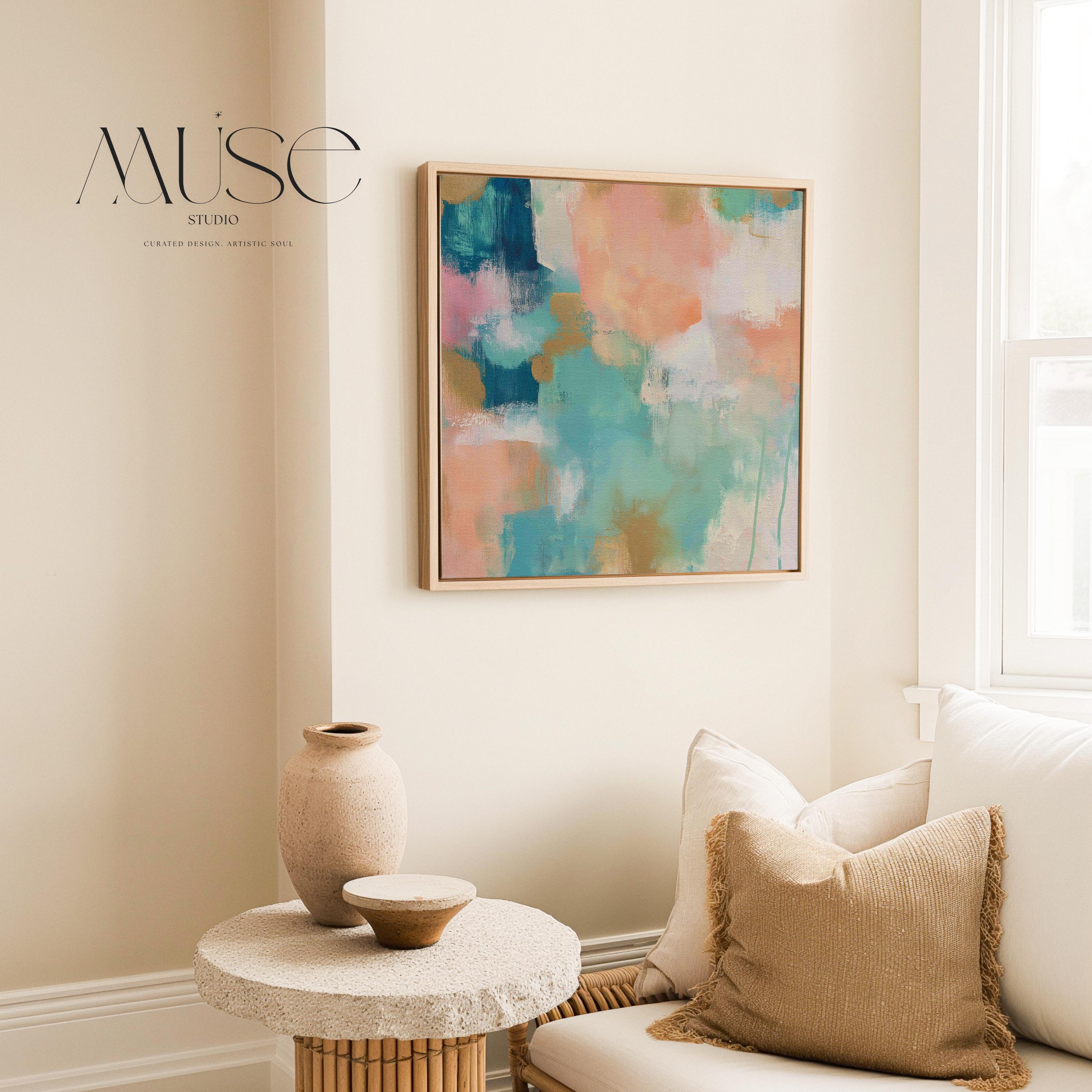 Large square abstract framed canvas wall art featuring coral, peach, teal, aqua blue, and warm sand tones layered over a soft cream background, styled above a neutral sofa, adding soft color contrast and airy painterly texture to a curated living space.