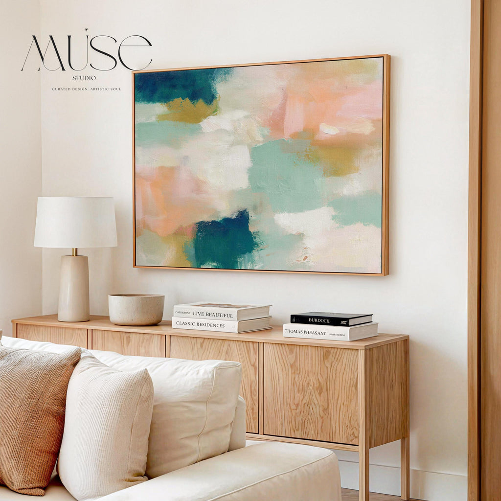 Large horizontal abstract framed canvas wall art featuring deep teal, mint green, soft peach, warm sand, and layered cream brushstrokes, styled above a neutral sofa, adding soft contrast and airy color balance to a curated living room.
