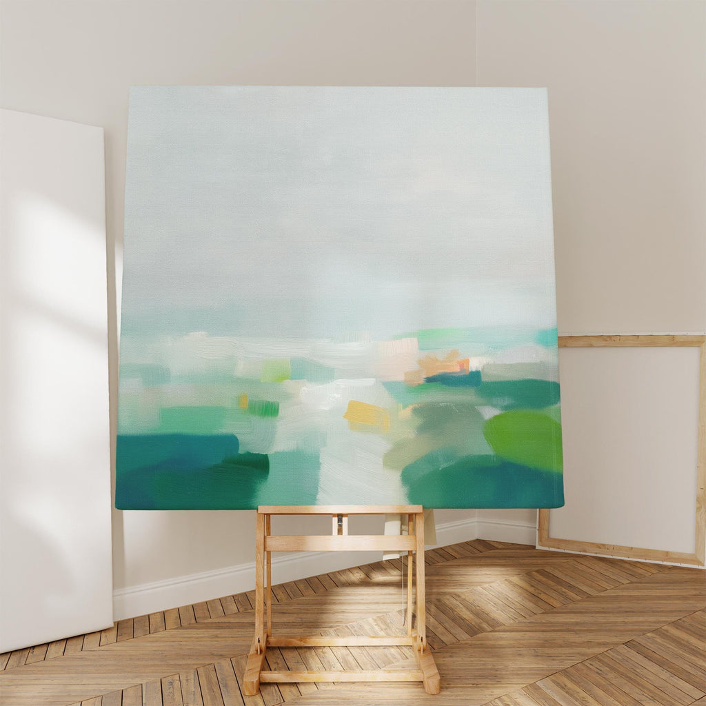 Large square abstract canvas wall art featuring soft green, aqua, and muted blue tones in a calming landscape composition, styled in a neutral interior to create an airy, refined focal point for living rooms or bedrooms.