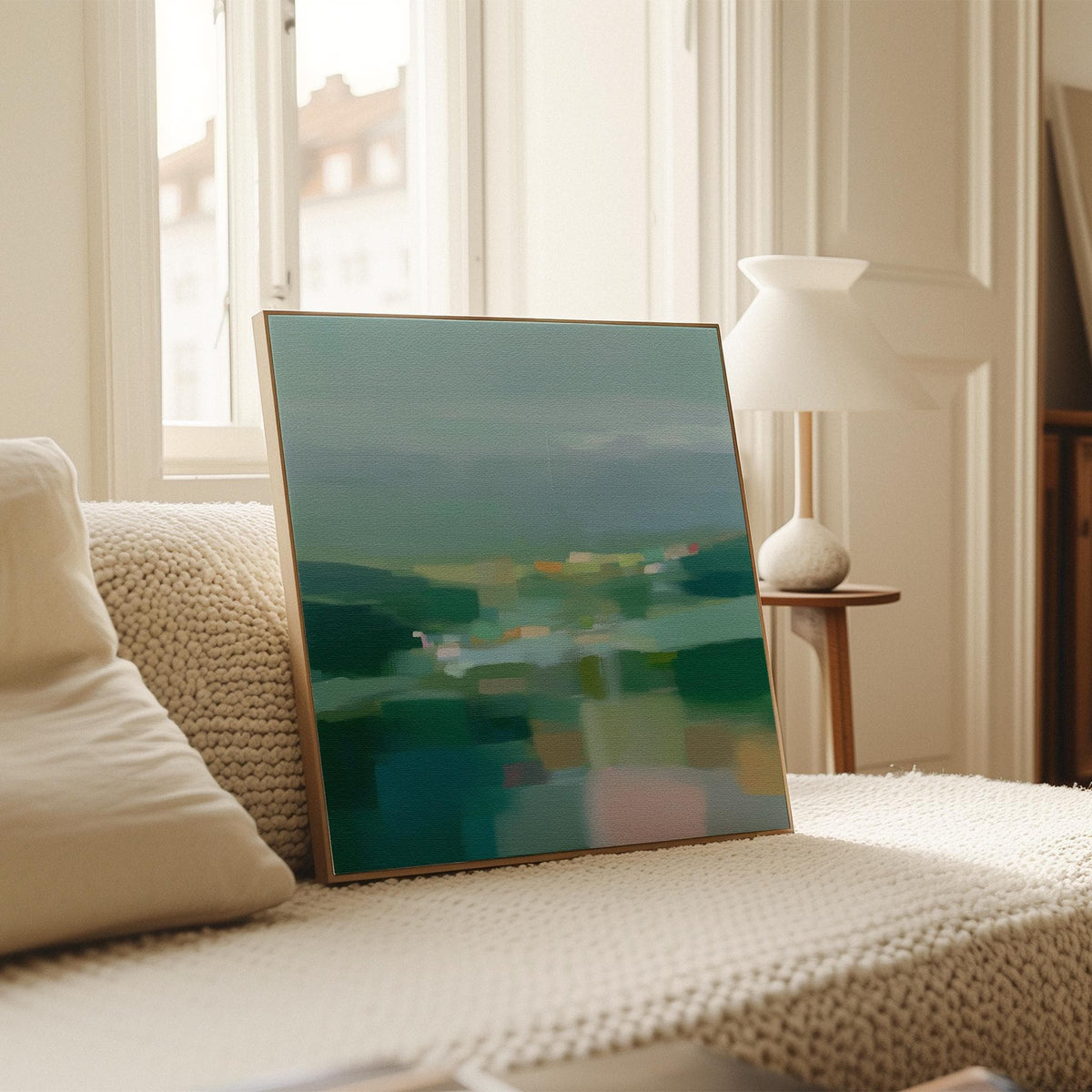 Large square framed canvas wall art in layered sage, deep green, and misty blue tones styled against a light neutral wall, creating a calm nature-inspired focal point in a refined interior.