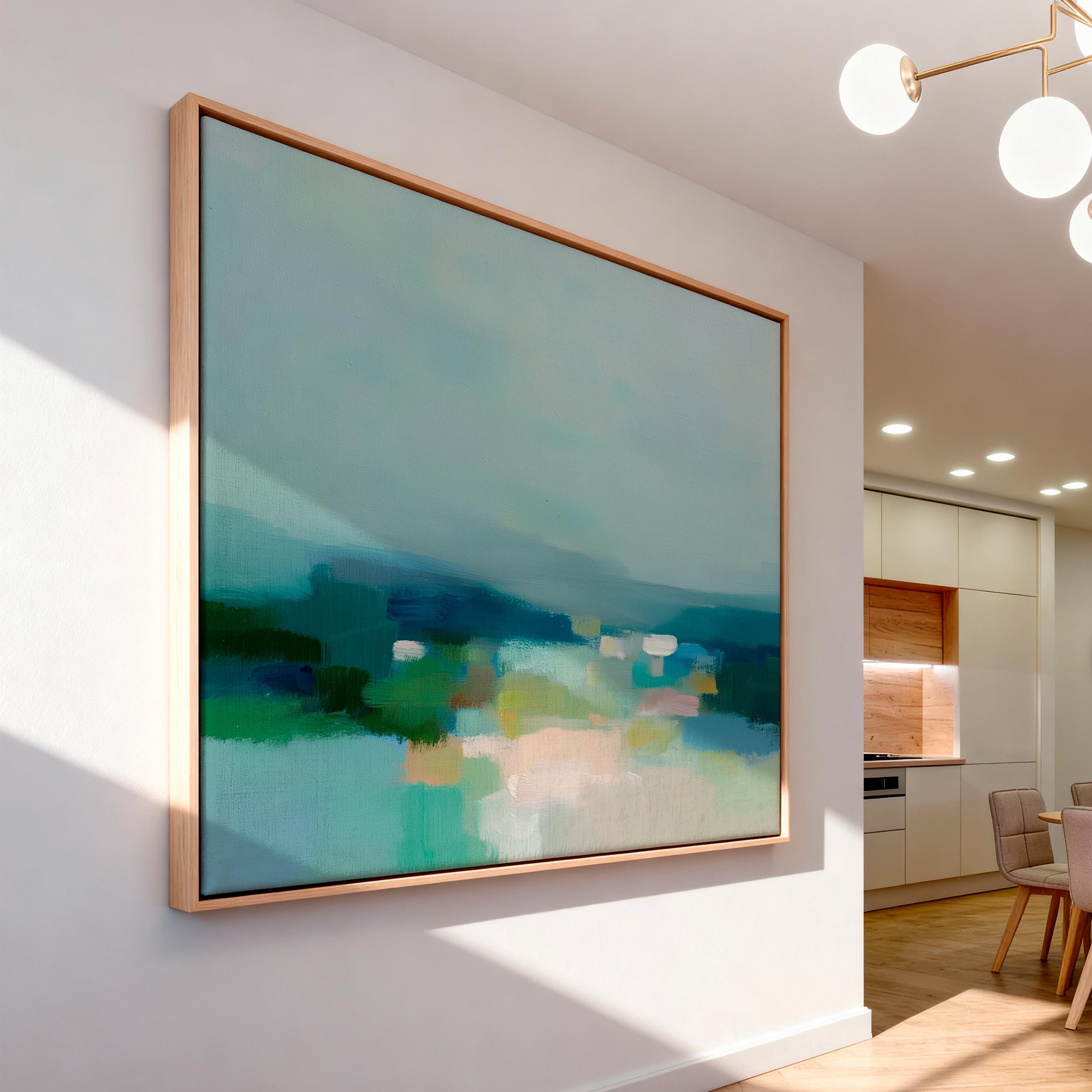 Large horizontal framed canvas wall art in sage green, deep teal, cream, and soft blue tones styled above a light wood console in a warm neutral interior, creating a calm landscape-inspired focal point.
