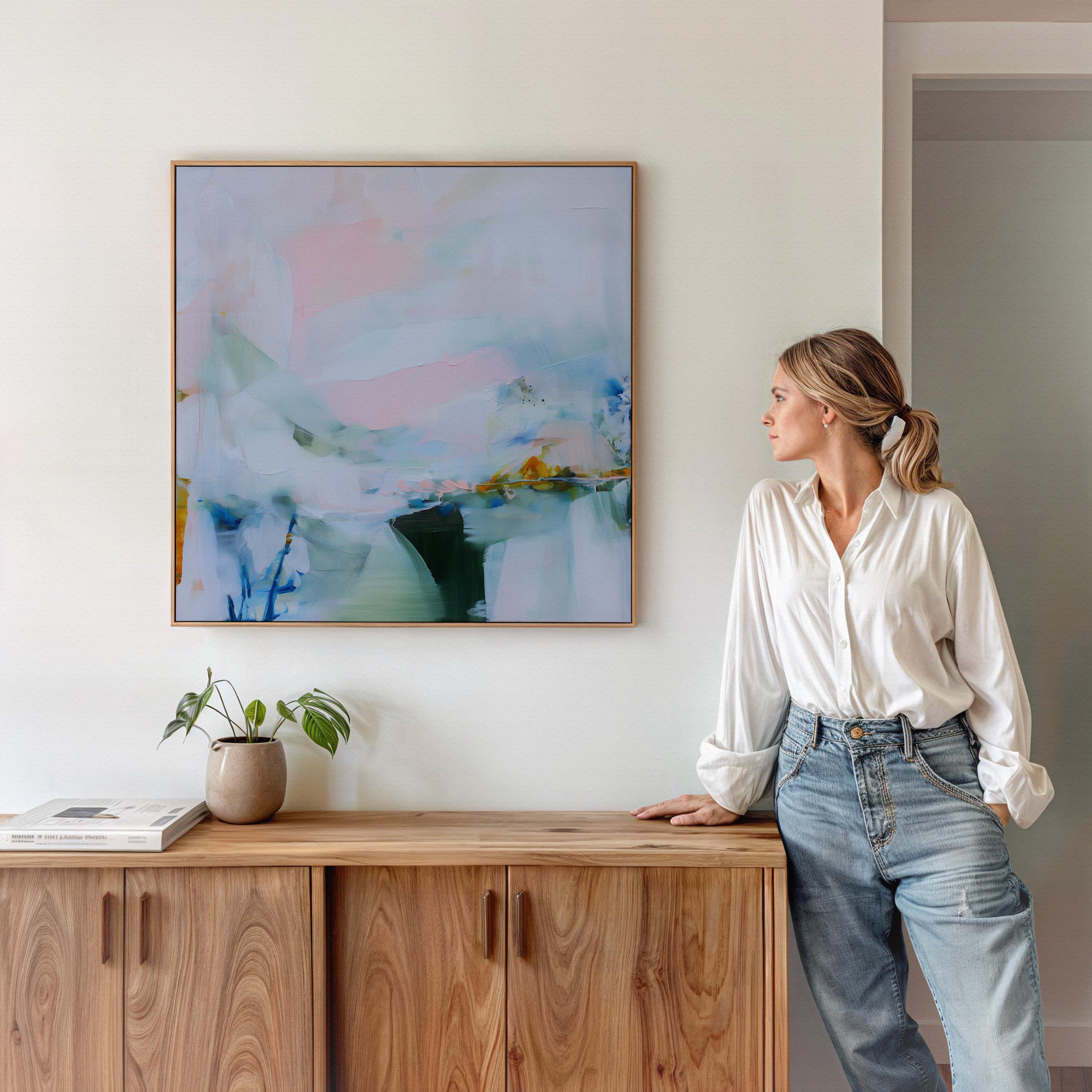 Muse Studio framed abstract wall art in soft blush, misted blue, pale sage, and deep teal with warm ochre accents, printed with museum-grade giclée inks on premium gallery-wrapped canvas, set in a natural wood float frame, styled above a neutral linen sofa in an organic transitional living room with warm oak tones and layered textures.