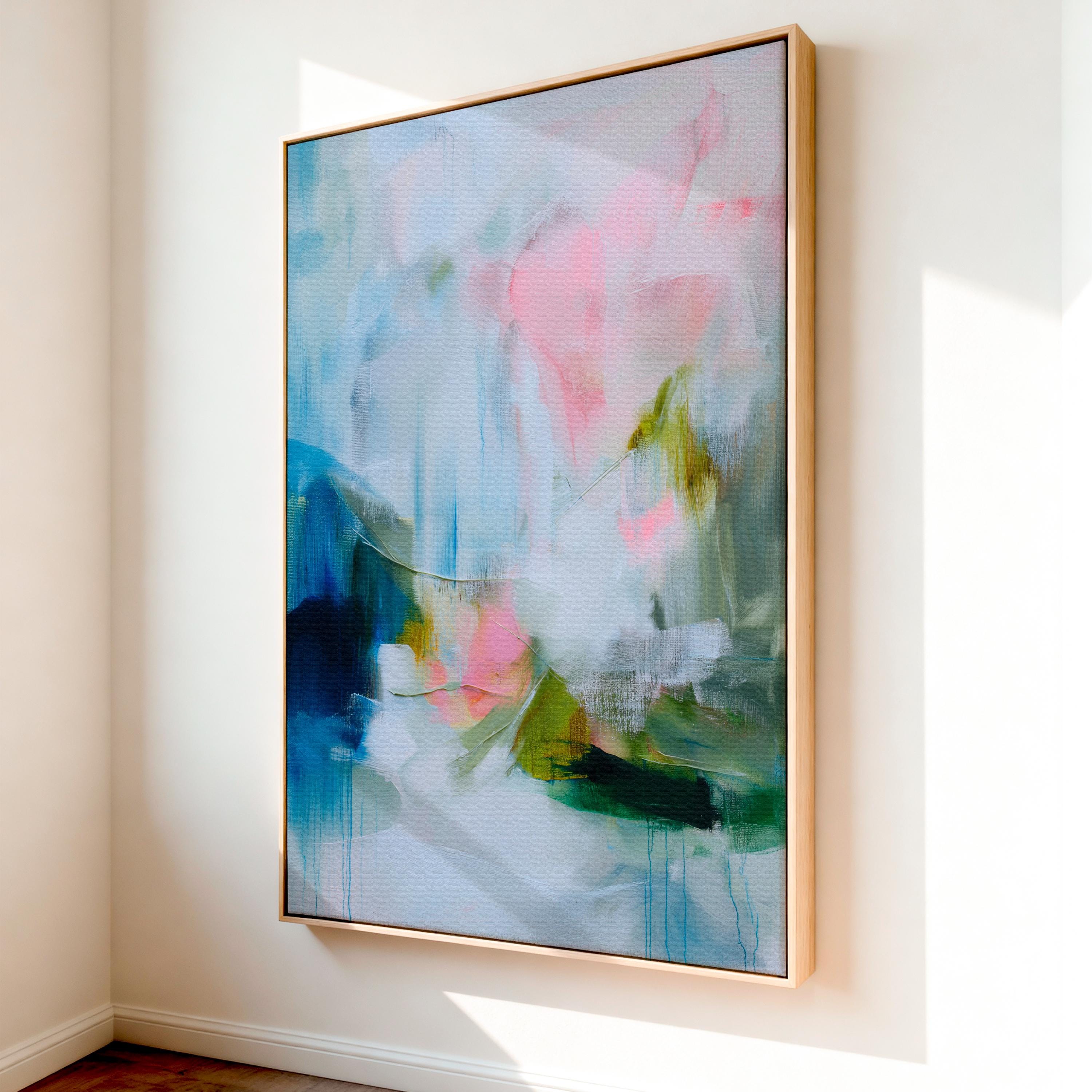 Spring Showers No. 1061 by Muse Studio & Co. vertical abstract wall art in blue, blush pink, and green tones, printed with museum-grade giclée inks on premium gallery-wrapped canvas and framed in natural wood float frame, styled in a serene bedroom above bed in soft contemporary interior.