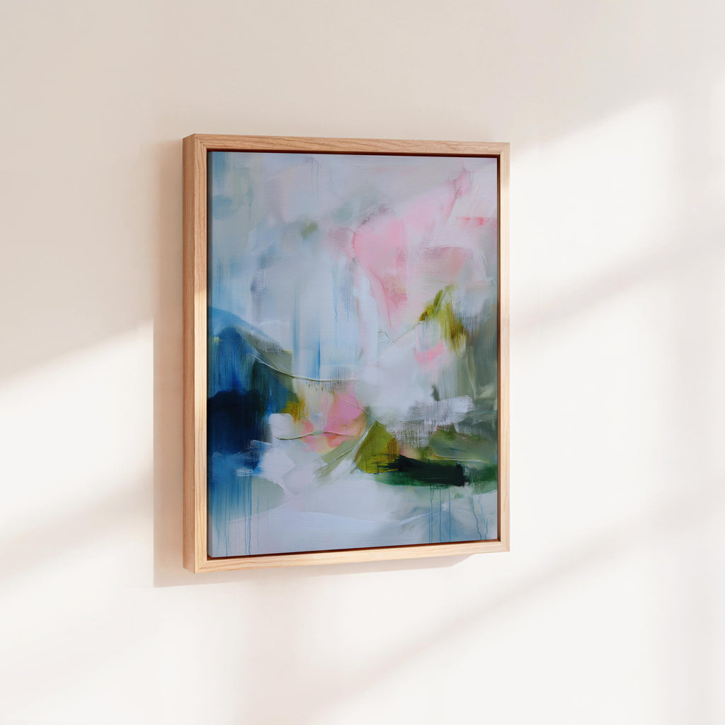 Spring Showers No. 1061 by Muse Studio & Co. vertical abstract wall art in blue, blush pink, and green tones, printed with museum-grade giclée inks on premium gallery-wrapped canvas and framed in natural wood float frame, styled in a serene bedroom above bed in soft contemporary interior.