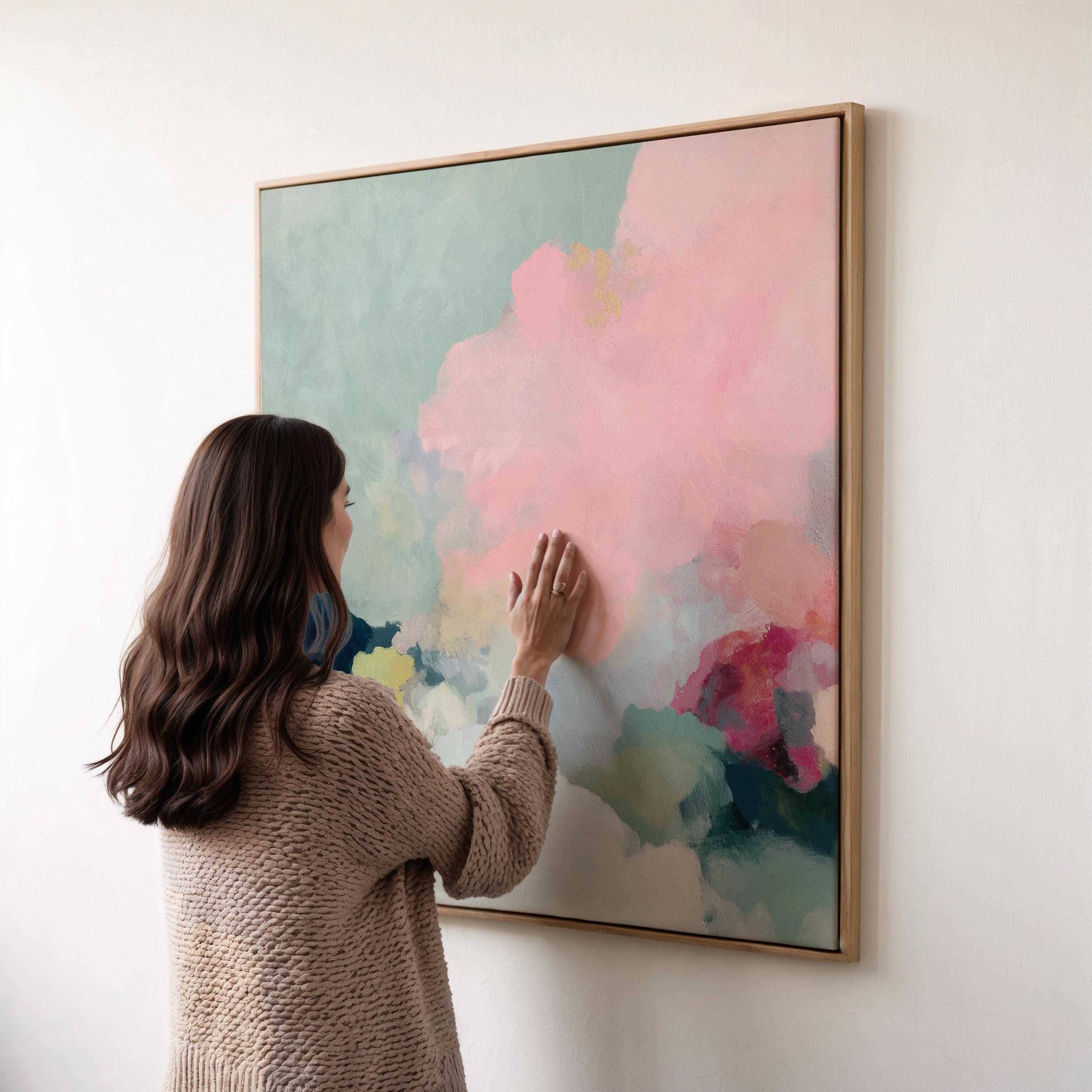 Square framed pastel abstract wall art by Muse Studio featuring blush pink cloud-like forms with soft green and cream tones. Printed with museum-grade giclée inks on premium artist canvas and finished in custom wood float frames in natural, white, black, or antique gold and silver, designed for bedrooms or serene living spaces.