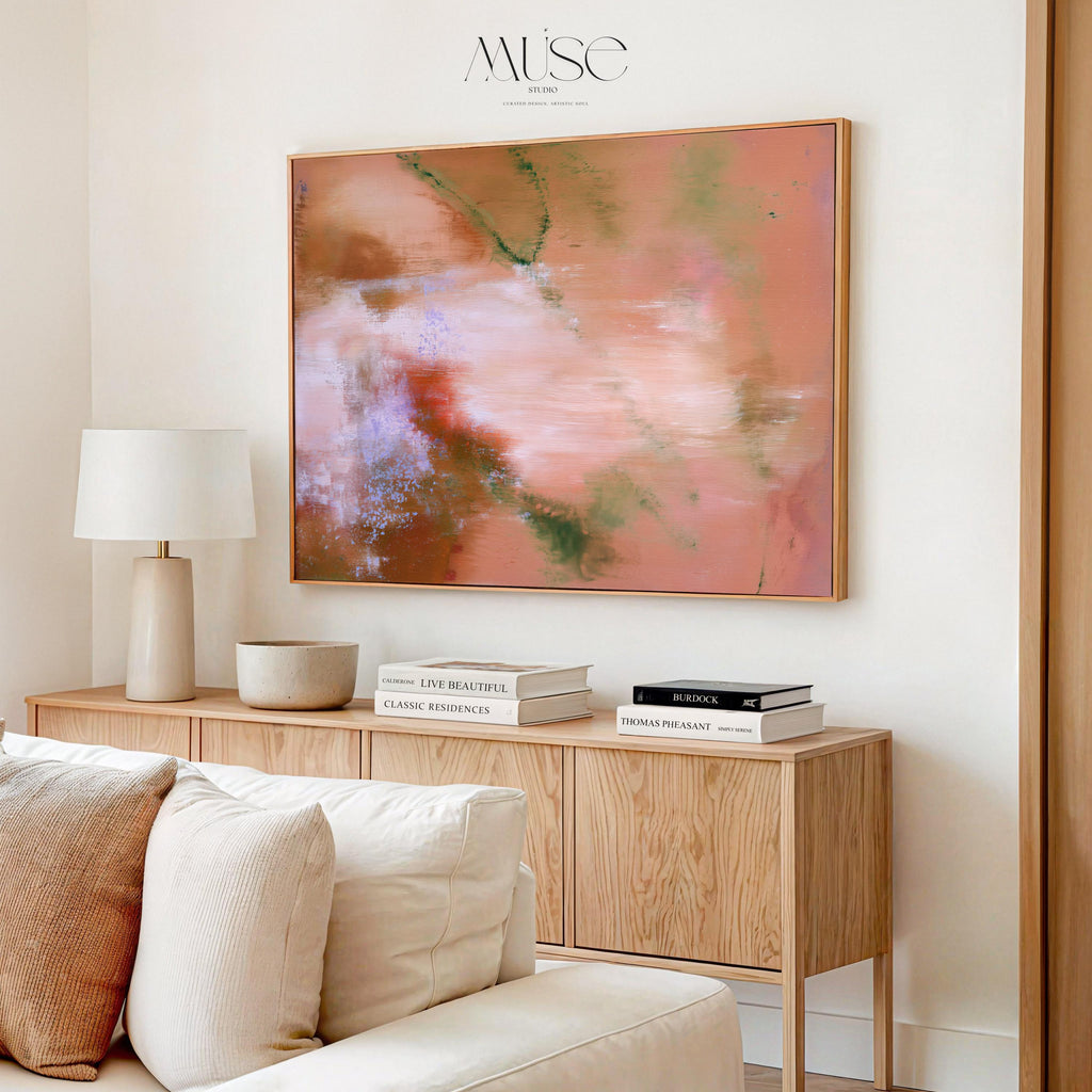 Large warm minimalist abstract wall art styled above a light oak wood credenza with ceramic lamp and books in an organic modern living room.