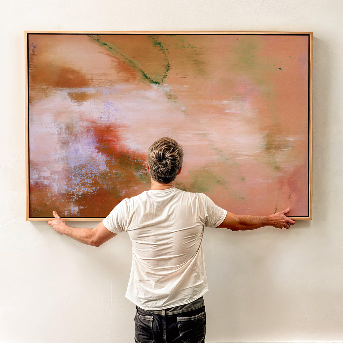Person holding a large horizontal framed terracotta abstract canvas art print against a light wall to demonstrate scale.